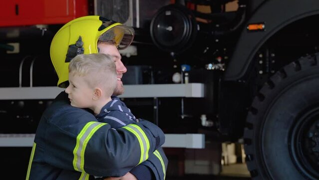 Brave firefighter in uniform hugs a little boy with a toy against a fire engine