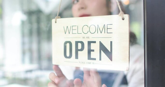 Business owner attractive Asian woman in apron hanging we're open sign on front door smiling welcoming clients to new cafe. startup Small Business, people and youth concept.