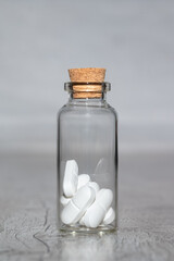 Glass vial with white pills on a wooden table. the Container on a grey background. 