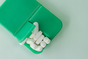 Some pills in a green pillbox on green background