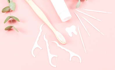 Bamboo toothbrush, dental floss, toothpicks, a tube of toothpaste and a paper tooth on a soft pink