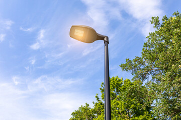 Modern lamppost with LED lamp on a summer day in a public park against the sky - obrazy, fototapety, plakaty