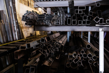 Variety of iron square tubes, round pipes and shaped profiles on rack in metalworking shop..