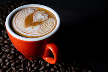 Latte coffee in red cup between coffee beans. With a copy space background.