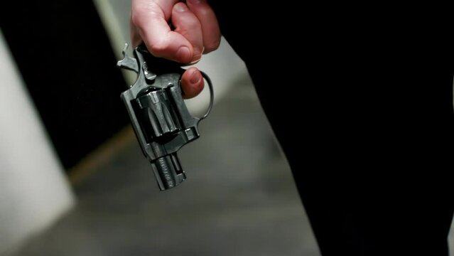 Close-up guy lowers his hand with revolver pistol to his leg in black pants, cocks the trigger by scrolling barrel of revolver and raises it, front view.