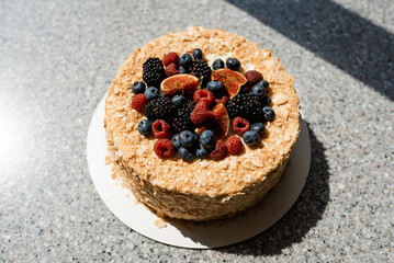 Savoyardi berry cake garnished with blackberries,blueberries and fresh figs on a wooden stand with hydrangea flowers on wooden table.Close up of cake in rustic style.