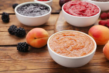 Different puree in bowls and fresh fruits on wooden table