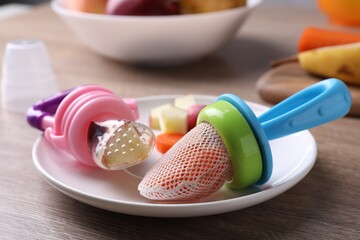 Different nibblers with fresh apple and boiled carrot on wooden table, closeup. Baby feeder