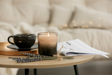 Beautiful candle, lavender, newspaper and cup on round wooden table in living room