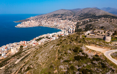 Fototapeta na wymiar Scenic aerial view of Sarande cityscape on shores of gulf of Ionian Sea and ancient Lekuresi Castle on hill above city on sunny spring day, Albania