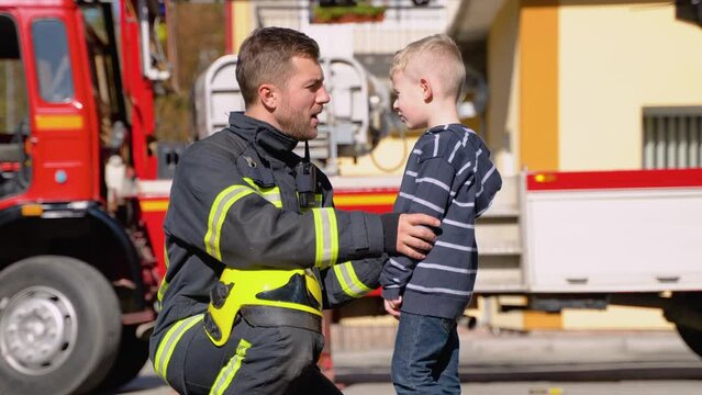 Little boy with firefighter in protective uniform in fire station