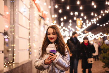 Happy young woman walking in city street during Christmas holidays at night