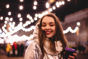 Cheerful happy young woman walking in city street during Christmas holidays at night
