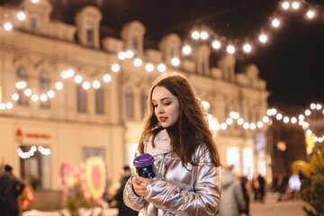 Thoughtful young woman walking in city street during Christmas holidays at night