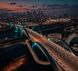 Aerial drone shot of 6th street bridge in Los Angeles, California with skyline behind it at night.