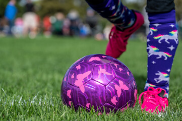 Selective focus on girls' soccer ball with a player on the grass field. 