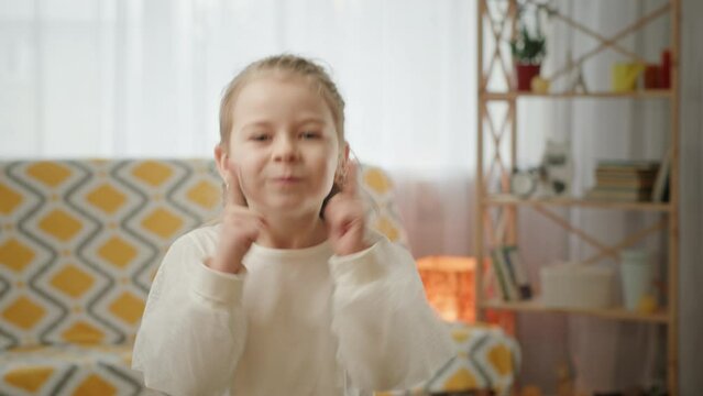 Funny girl blowing cheeks. Static shot of cute girl puffing and touching cheeks while grimacing near sofa in living room at home