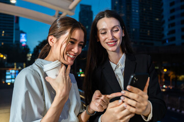 Caucasian businesswoman and Asian worker stand outdoor in city at night. 