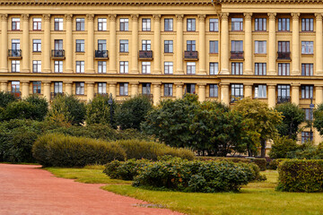 Naklejka premium Facade of a yellow building with windows and balconies, next to a park. European house with columns.