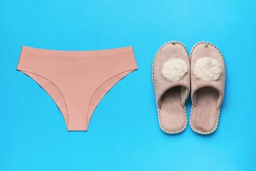 Türaufkleber Women's panties and warm slippers on a blue background. Minimal concept of women's accessories. © kvladimirv