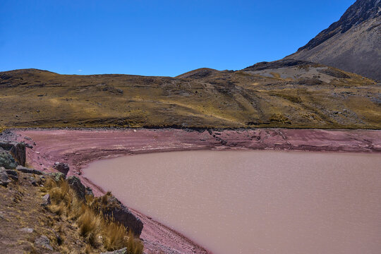 Laguna roja ubicada en medio de un valle andino con un cielo celeste 