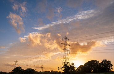 silhouette of high voltage power lines against a colorful sky at sunrise or sunset.