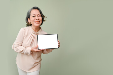 Happy aged-asian woman showing a blank screen tablet mockup, isolated over green background.