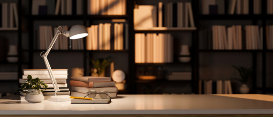 Empty copy space on tabletop with books and table lamp over blurred bookshelves in the background. © bongkarn