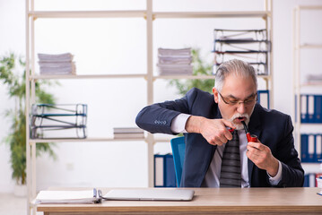 Old male employee smoking pipe at workplace
