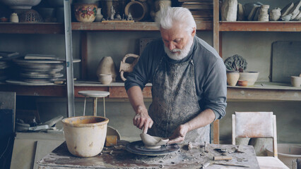 Creative male sculptor is making unusual broad bowl while standing at working table in his...