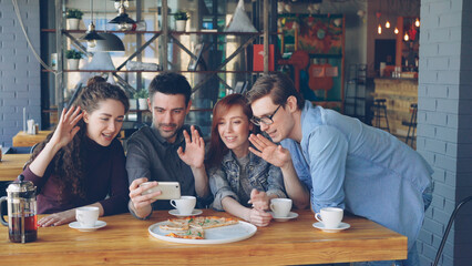 Young people are having funny video chat holding smartphone looking at webcam chatting to friend at...