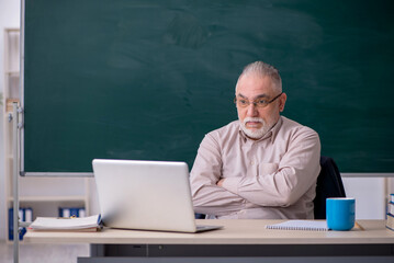 Old male teacher in front of blackboard