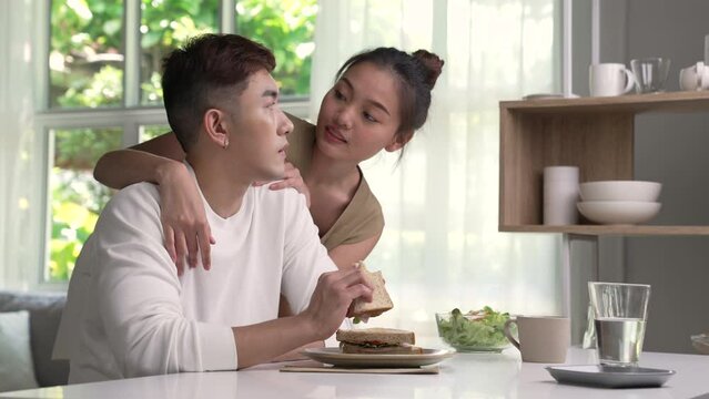 Loving young Asian couple looking at each other while having breakfast. Close up shot of young man and woman having meal at home. Happy young couple eating.