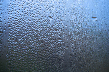 Drop of water on glass close-up. Sweaty window, rain. Blue background.