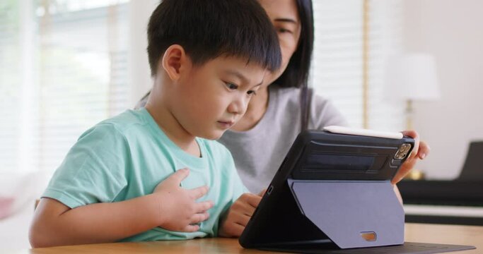 Cute asia people alpha Gen Z kid small boy play video game app online happy mum at home. Enjoy Child care fun class little son and mom study learn upskill idea course on smart digital tablet computer.