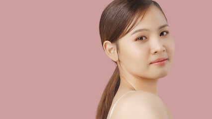 Close up portrait beauty shot of Beautiful Asian girl looking at camera isolated on pink background with copy space.