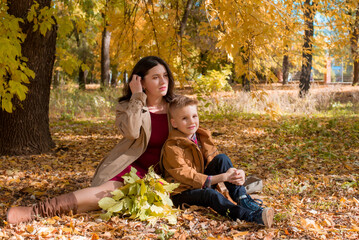 Young mother with dark hair in a beige autumn raincoat with her son in a sunny autumn park. Autumn walk in the park. Autumn mood. Motherhood. time together