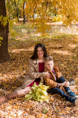 Young mother with dark hair in a beige autumn raincoat with her son in a sunny autumn park. Autumn walk in the park. Autumn mood. Motherhood. time together