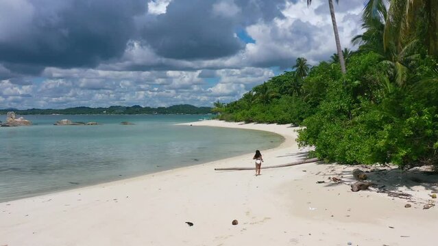 aerial of young asian girl running on empty white sand beach on tropical island in belitung indonesia