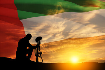 Silhouette of soldier kneeling with his head bowed against the sunrise or sunset and UAE flag....