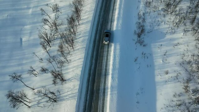 Aerial view tracking a car driving on a slippery, winter road in Lapland - high angle, drone shot