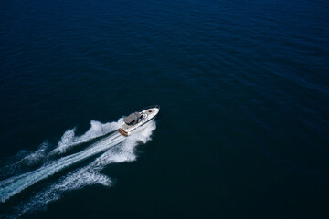 a high-speed big boat with people moves quickly on dark blue water making a white trail behind the boat.