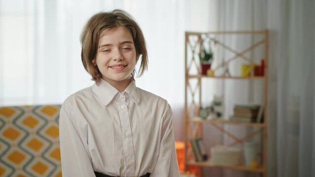 Shaggy schoolgirl sits smiling cutly and blinking innocently