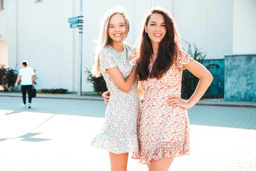 Portrait of two young beautiful smiling hipster female in trendy summer white sundress.  carefree women posing on street background. Positive models having fun, hugging and going crazy