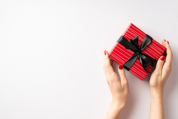 Black friday sales concept. First person top view photo of girl's hands holding red giftbox with black ribbon bow on isolated white background with empty space