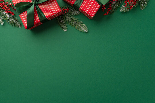 New Year concept. Top view photo of red gift boxes with green ribbon bows mistletoe berries and pine branches in frost on isolated green background with copyspace