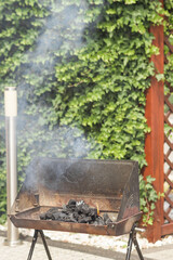 Smoke over flaming pile of charcoal in metal brazier on backyard. Folding portable brazier filled with burning coal.