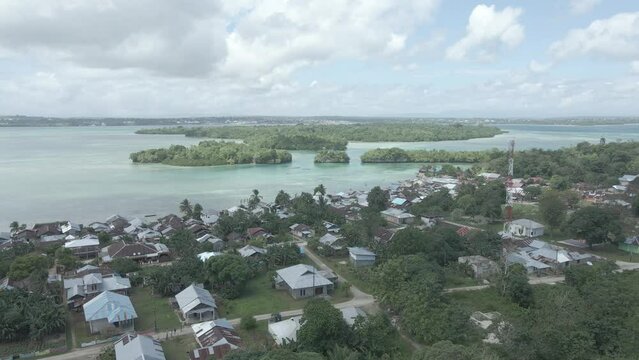 Aerial view of village near beautiful beach with small island in the background in Maluku, Indonesia