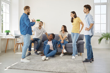 Friends meeting at home. Young people gather in living room, talk, listen to each other, discuss different things. Group of diverse friends listening to man telling story and explaining what happened - obrazy, fototapety, plakaty