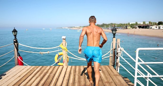 Rear view of young sports man jumping into sea from jetty